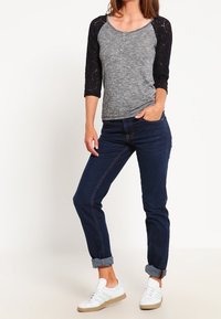 Top grigio e nero con maniche a tre quarti e dettagli in pizzo, abbinato a jeans scuri arrotolati e sneakers bianche con accenti verdi.