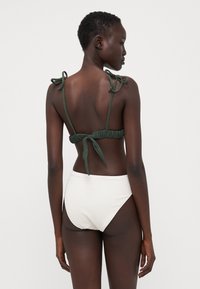 Top bikini verde con lacci, abbinato a slip bianchi a vita alta con texture. Design minimalista con tessuto morbido.