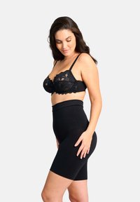 Zwarte kant bralette met verstelbare banden en gegolfde randen, gecombineerd met hoge zwarte shapeshorts met een gladde textuur.