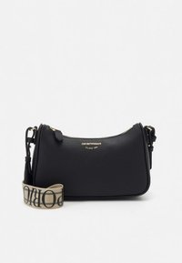 Zwarte leren crossbodytas met een gestructureerde afwerking, gouden hardware en een beige band met merknaam. Heeft een afgeronde vorm en een ritssluiting.