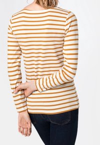 Koszula z długim rękawem z poziomymi paskami w kolorze musztardy i kremowym. Miękka tkanina, okrągły dekolt, dopasowany krój. Noszona z ciemnymi jeansami.