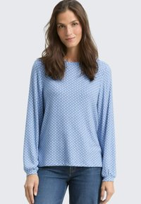 Hellblauses Langarmhemd mit geometrischen Mustern, weichem Stoff, rundem Halsausschnitt und gerafften Manschetten. Kombiniert mit blauen Jeans.