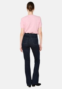Jeans acampanados de color azul oscuro con cintura alta, combinados con una blusa de punto de manga corta en rosa claro. Textura suave con detalles de costura visibles.