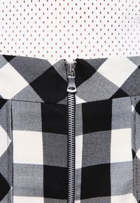 Černobílá kostkovaná sukně s viditelným stříbrným zipem, vyrobená z látky s texturovaným povrchem a kontrastním geometrickým vzorem.