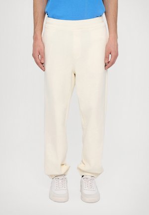 Cream fleece joggers with a relaxed fit, elastic waistband, and gathered cuffs, paired with white sneakers. Soft texture, simple design.