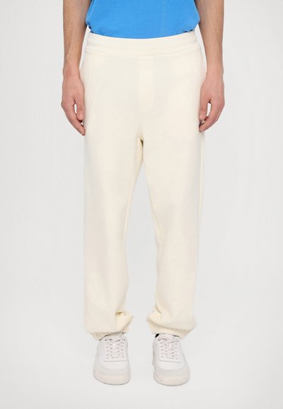 Jogging en polaire crème avec une coupe décontractée, taille élastique et poignets froncés, associés à des baskets blanches. Texture douce, design simple.