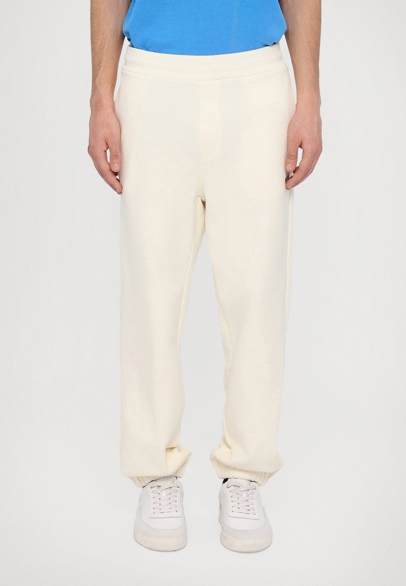 Cream fleece joggers with a relaxed fit, elastic waistband, and gathered cuffs, paired with white sneakers. Soft texture, simple design.