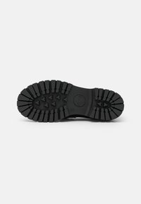 Black rubber shoe sole featuring deep treads, a round logo at the heel, and a textured surface for traction.
