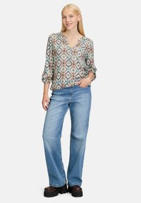 Printed blouse with a v-neckline and button detail, paired with light blue wide-leg jeans. Brown platform shoes. Patterns feature diamonds and lines.