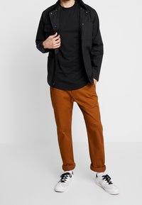 Black zip-up jacket with pockets, black t-shirt, orange rolled-up pants, and white sneakers with black laces. Casual outfit.