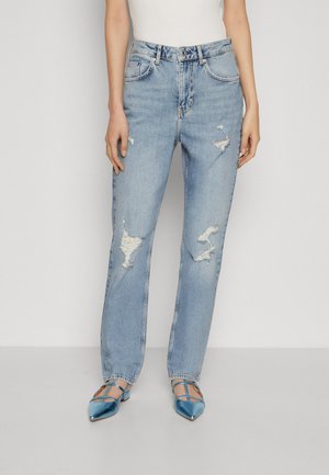 Jeans in denim azzurro chiaro con vestibilità rilassata, in evidenza con patch strappati e una finitura leggermente sbiadita. Abbinati a ballerine blu a punta.