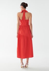 Punane puuvillane maksikleit kaeluse ja lipsusõlmega, millel on kihtide disain ja kroogitud ülakeha. Täiendatud kontsakingadega.