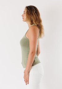 Canottiera slim-fit verde oliva realizzata in morbido misto cotone, con spalline sottili e superficie liscia. Indossata con pantaloni bianchi attillati.