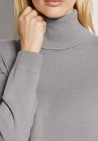 Hellgrauer Rollkragenpullover aus geripptem Strickmaterial, mit einem engen Sitz am Kragen und an den Bündchen. Glatte Textur.