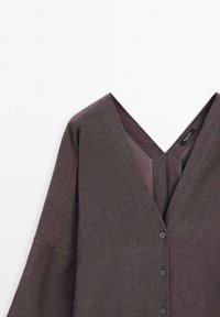 V-Ausschnitt, langärmliges Oberteil aus einem strukturierten, dunkelvioletten Stoff mit Knopfleiste und lockerer Passform. Verfügt über subtile Farbvariationen.