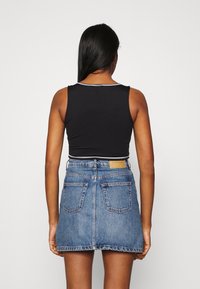 Svart ärmlös topp i kombination med en blekt blå denimminikjol med midjebandsetikett och bakfickor, vilket framhäver en avslappnad design.