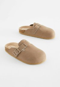 Beige ruskindslapper med rund tå, sidespænde og korksål. Tekstureret overflade og gummisål for greb og holdbarhed.