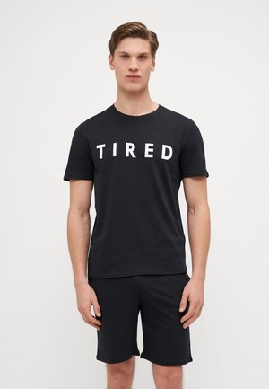 Black cotton t-shirt with short sleeves featuring the text "Tired" in large white block letters. Paired with matching black shorts.