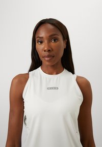 Vit ärmlös träningstopp i slät tyg, med en diskret Nike-logotyp i grått på bröstet.