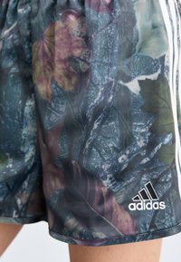 Zöld és barna árnyalatokban pompázó, levélszerű, többszínű mintázatú rövidnadrág, rugalmas derékpánttal és fehér Adidas logóval.