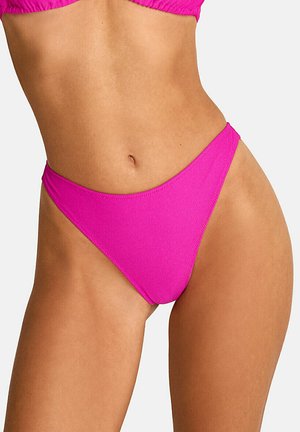 Torso de femme portant un bas de bikini côtelé rose vif et un haut assorti, fond blanc uni.