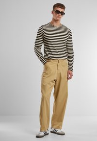 Striped long-sleeve shirt in black and cream, paired with khaki chinos. Model wears black sunglasses and brown athletic shoes with white accents.