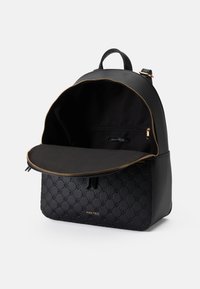 Mochila preta feita de material texturizado, apresentando um fecho dourado, interior espaçoso e um detalhe de logótipo na frente.