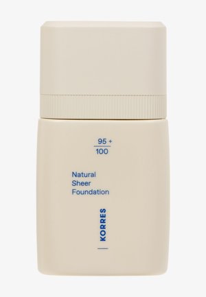 Beige flaske med mat finish og et rundt låg. Har blå tekst, der mærker produktet som "Natural Sheer Foundation" af Korres.