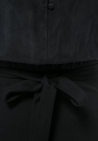 Tissu noir noué en nœud à la taille avec un superposé boutonné au-dessus, montrant un gros plan des détails et de la texture du vêtement.