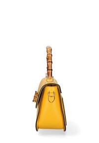 Borsa in pelle gialla con manico in bambù, bordi neri a contrasto, forma trapezoidale e una piccola tasca laterale con dettagli in metallo.