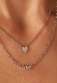 Colliers en argent superposés avec un charme en forme de cœur et un pendentif en forme de mot « Love », tous deux avec des surfaces lisses et des maillons de chaîne.