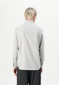 Stripete langermet skjorte i lysegrått og hvitt, med standard krage, knappede mansjetter og en lett buet skjortehem. Bakview vist.