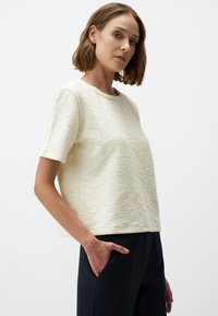 Crème-kleurige textuur short-sleeve top met een ronde halslijn, gemaakt van een zacht, pluizig materiaal, gecombineerd met donkere, op maat gemaakte broeken.