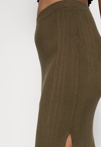 Stickad olivgrön midiklänning med vertikal ribbning, med en sidoklyvning och en åtsittande midja för en strukturerad silhuett.