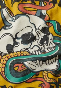 Graphic T-shirt featuring a skull entwined with colorful snakes. Predominantly yellow background with bold black, green, and red accents.