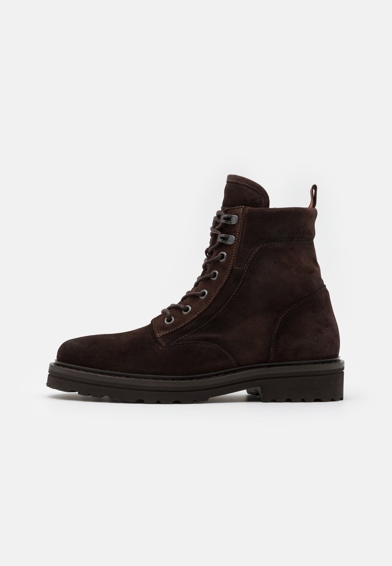 Botte à lacets en daim brun foncé, avec semelle épaisse à crampons et languette à l'arrière, présentée de profil sur fond blanc.