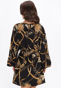Fekete ruha arany lánccal és virágmintákkal, hosszú ujjú, deréknál megkötött, kerek nyakkivágással. Sima anyagtextúra.