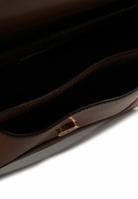 Interieur van een bruine leren handtas met een gladde textuur, voorzien van twee compartimenten en een sluiting met een goudkleurige knop.