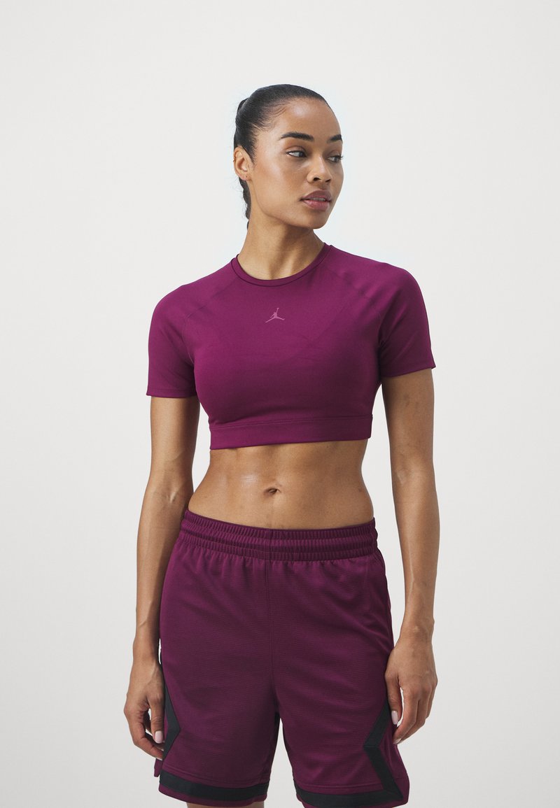 Maronfarbenes, kurzes Sporttop mit kurzen Ärmeln und glatter Textur, kombiniert mit maronfarbenen Shorts mit schwarzen Akzenten und einem elastischen Bund.