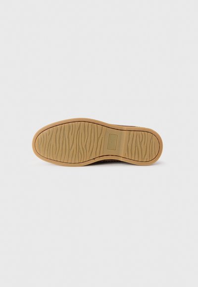 Sole in gomma con una texture ondulata beige. Presenta un'etichetta di branding rettangolare vicino al tallone. Design piatto e resistente.