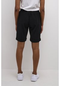 Czarne szorty o luźnym fasonie, z podwiniętymi mankietami, elastycznym paskiem i lekkim materiałem. Połączone z białymi sneakersami.