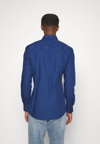 Camicia di cotone blu navy con maniche lunghe, colletto standard e orlo curvo. Caratterizzata da polsini con bottone e una texture liscia.