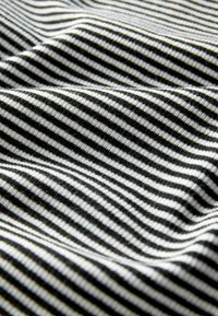 Nahaufnahme von schwarz-weiß gestreiftem Stoff mit sichtbarer gerippter Textur und sanften Falten, die weiche Schatten erzeugen.
