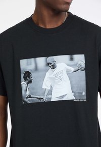 T-shirt noir en coton avec un grand graphisme noir et blanc représentant deux personnes jouant au basket-ball.