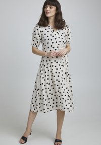 Vestido cruzado en crema con lunares negros, que presenta mangas cortas abullonadas, un lazo en la cintura y una longitud midi fluida. Tela suave y liviana.