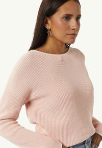 Light pink knitted sweater with a wide neckline, ribbed texture, and long sleeves, featuring a contrasting white trim along the neckline.