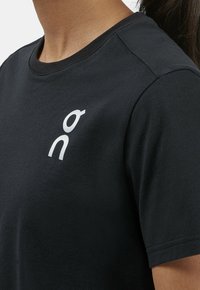 Black cotton t-shirt with a round neckline. Features a small, white logo on the left chest. Short sleeves with a smooth texture.