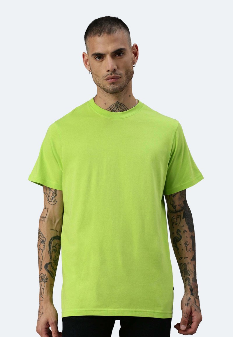 T-shirt in cotone verde neon con maniche corte, colletto rotondo e vestibilità rilassata. Presenta tatuaggi visibili sulle braccia.