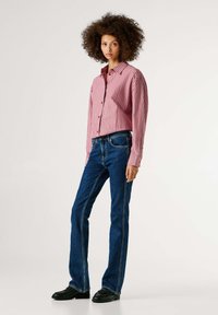 Sarkani un balti svītraini pogājama krekls ar garām piedurknēm, savienots ar tumši zilām izpletuma džinsu biksēm un melnām kurpēm. Vienkāršs dizains, ikdienišķs piegriezums.