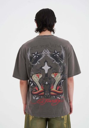 Grijze oversized t-shirt met een kleurrafische afbeelding van twee slangen, vleugels en sterren op de achterkant. Korte mouwen en een ronde halslijn.